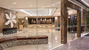 Een moderne lobby met een marmeren receptiebalie, een groot abstracte sculptuur en een glazen scheidingswand.