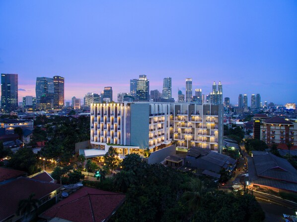 A high-rise hotel with multiple balconies, surrounded by dense urban cityscape at dusk. - Ayaka Suites (Jakarta)