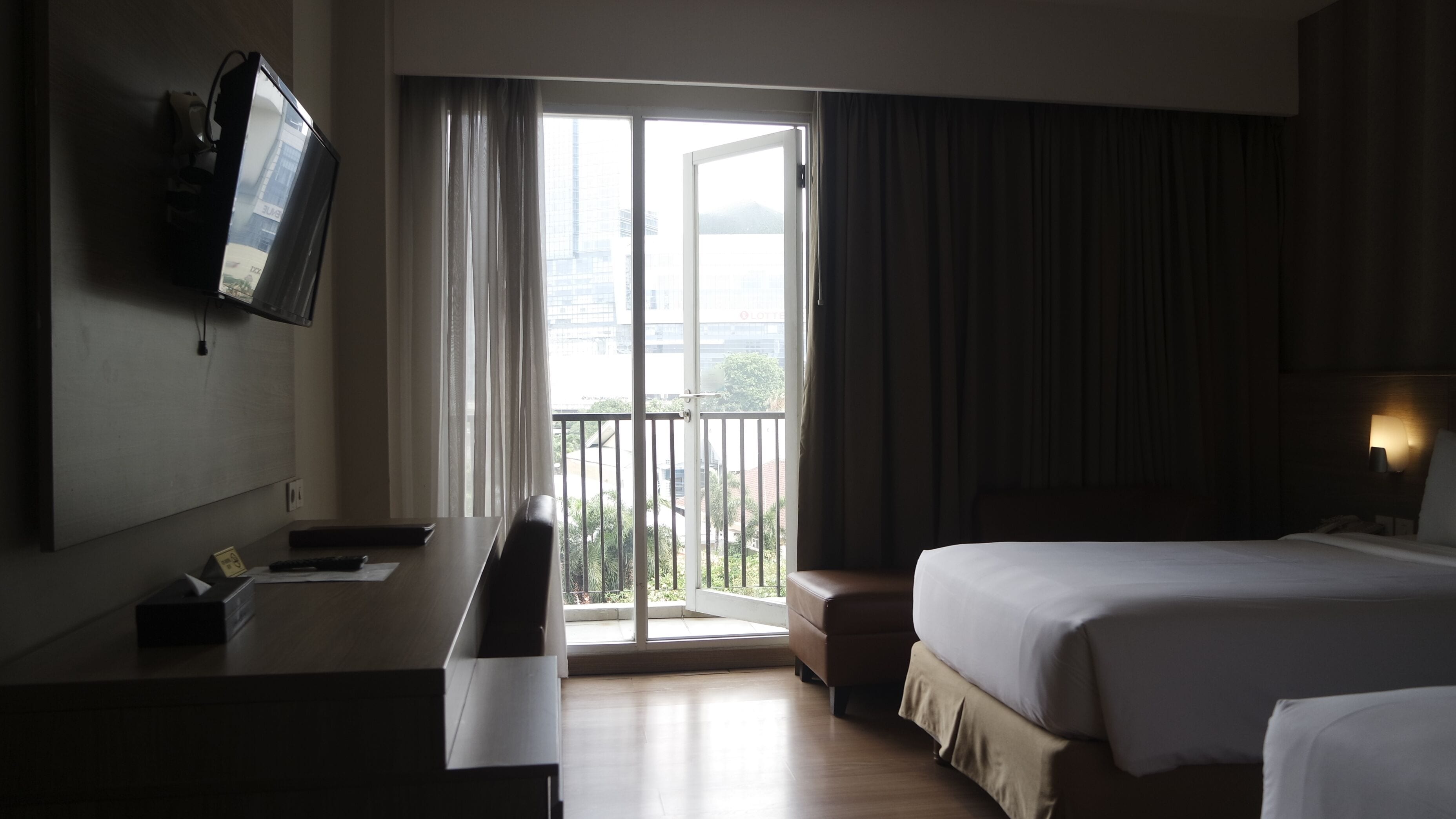 Ein Hotelzimmer mit Bett, Schreibtisch, Fernseher und einem Balkon mit Vorhängen.