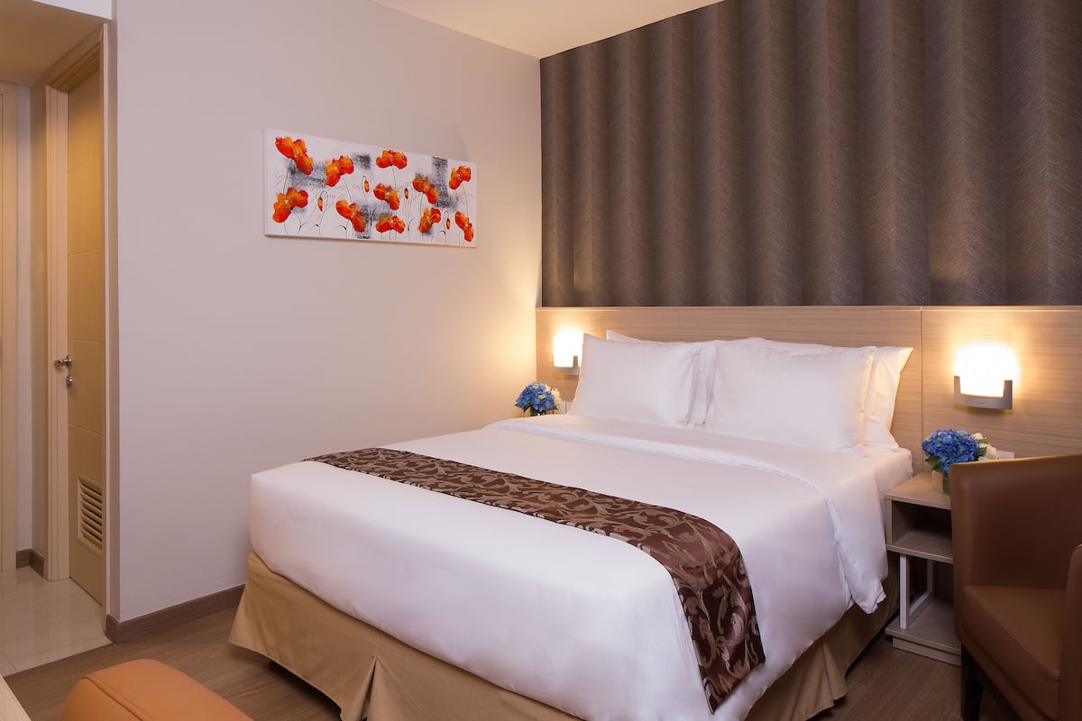 Ein ordentlich bezogenes Bett mit weißen Leinen und braunen Akzenten, ein an der Wand befestigtes Kunstwerk mit roten Blumen und ein brauner Vorhang.