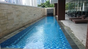 A swimming pool with a tiled edge, surrounded by a stone wall and glass windows. - Ayaka Suites (Jakarta)