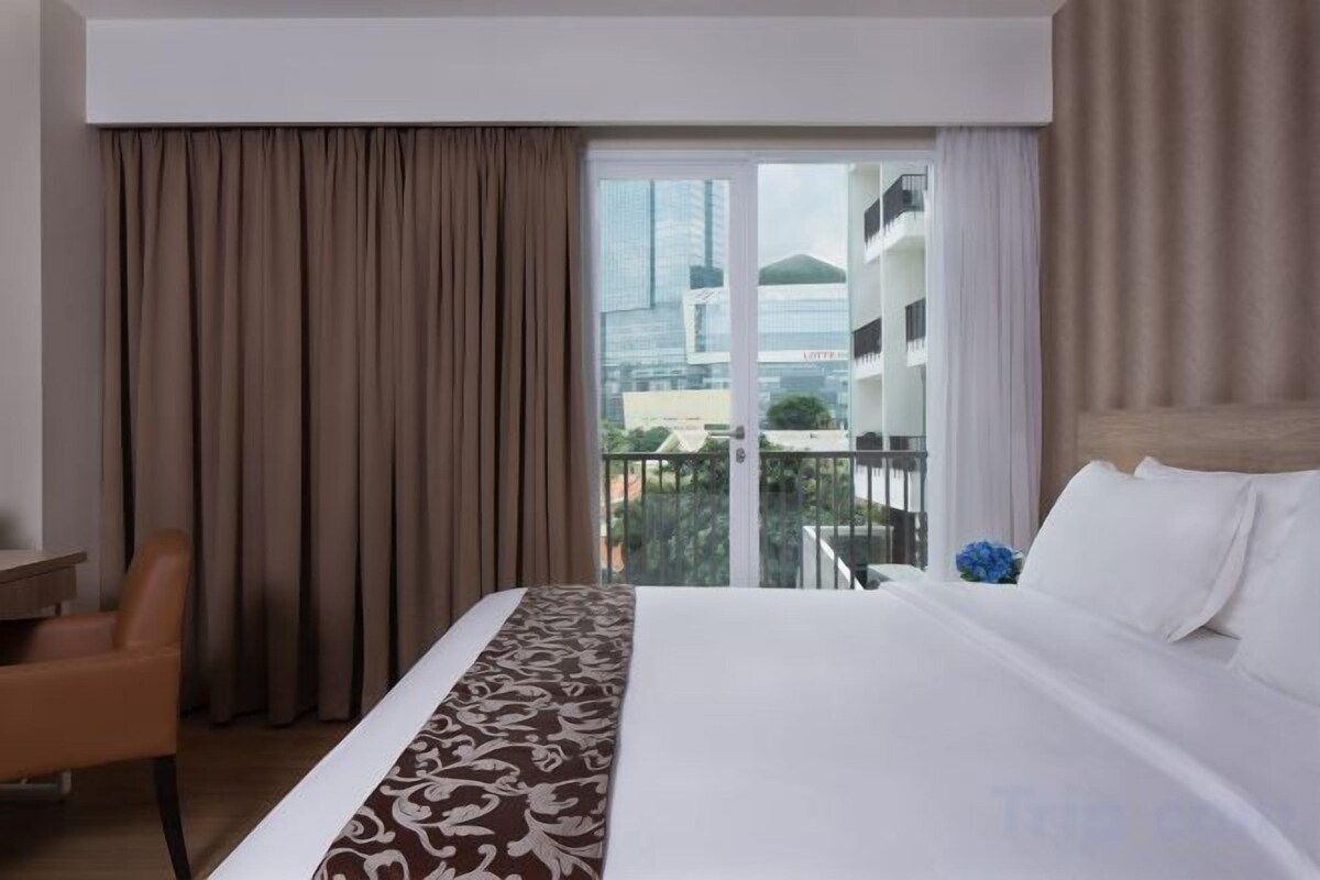 A hotel room with a large bed, a chair, and a view of the city through a sliding door.