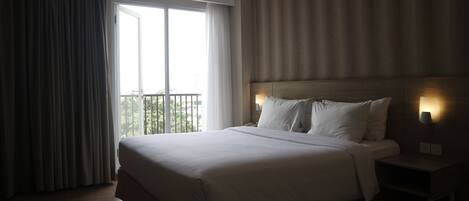 Habitación de hotel con una cama grande, una mesita de noche, una lámpara de pared y vista a zonas verdes.