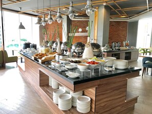 A buffet setup with various food items, a brick wall, and hanging pendant lights. - Ayaka Suites (Jakarta)