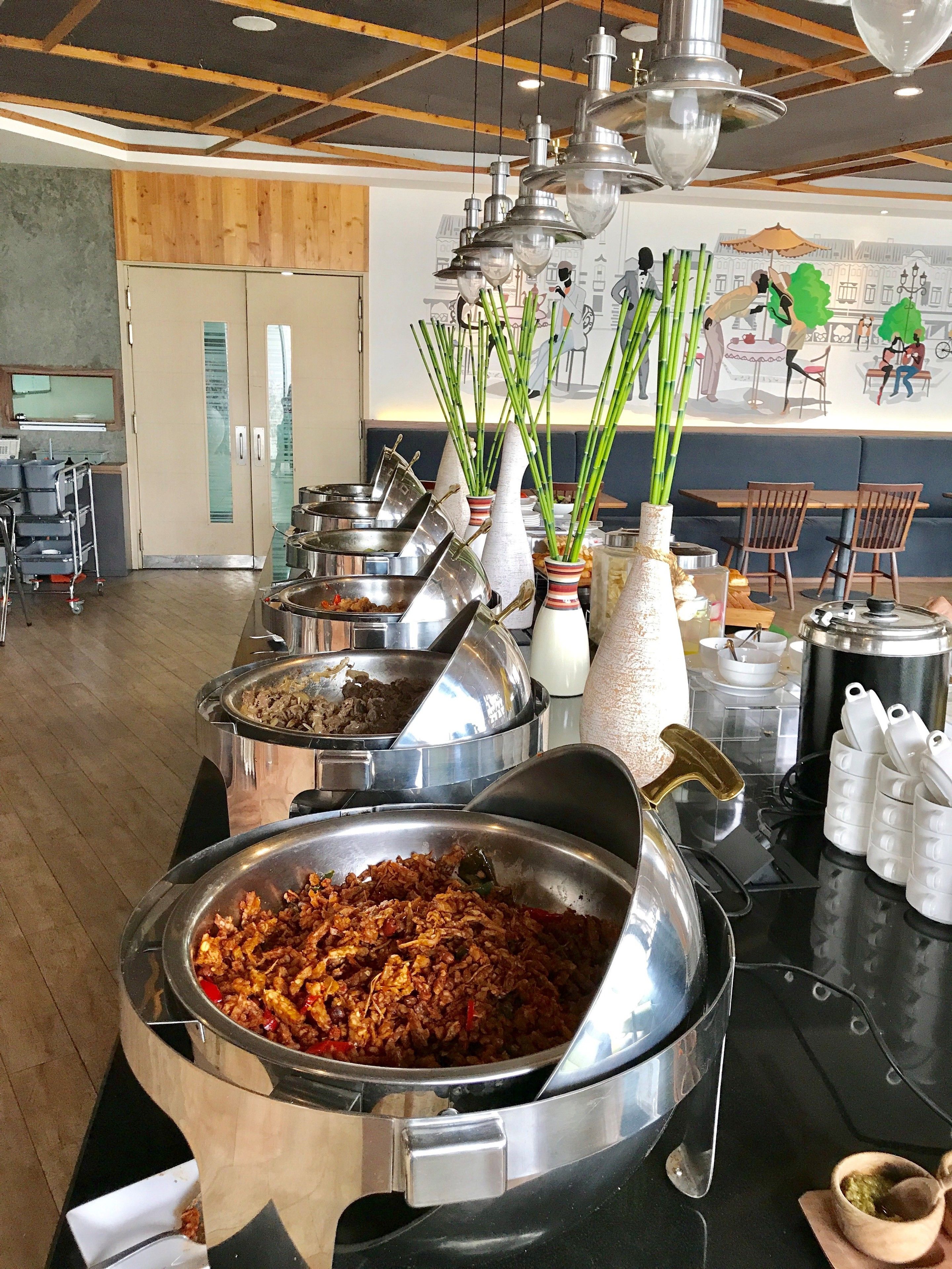 A buffet area with various food containers and a mural on the wall.