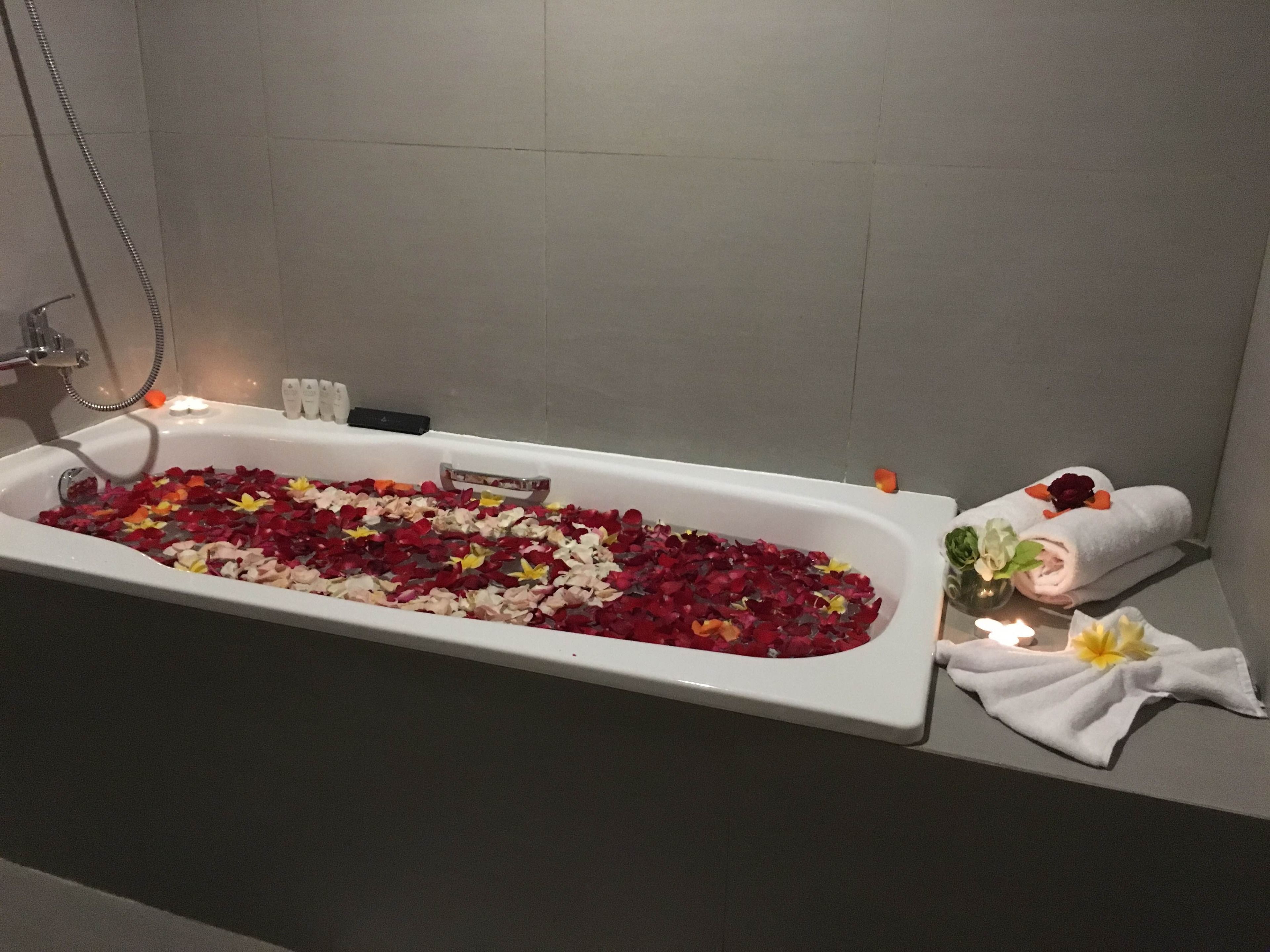 Une baignoire remplie de pétales de rose et de fleurs, avec des serviettes et une bougie à proximité.