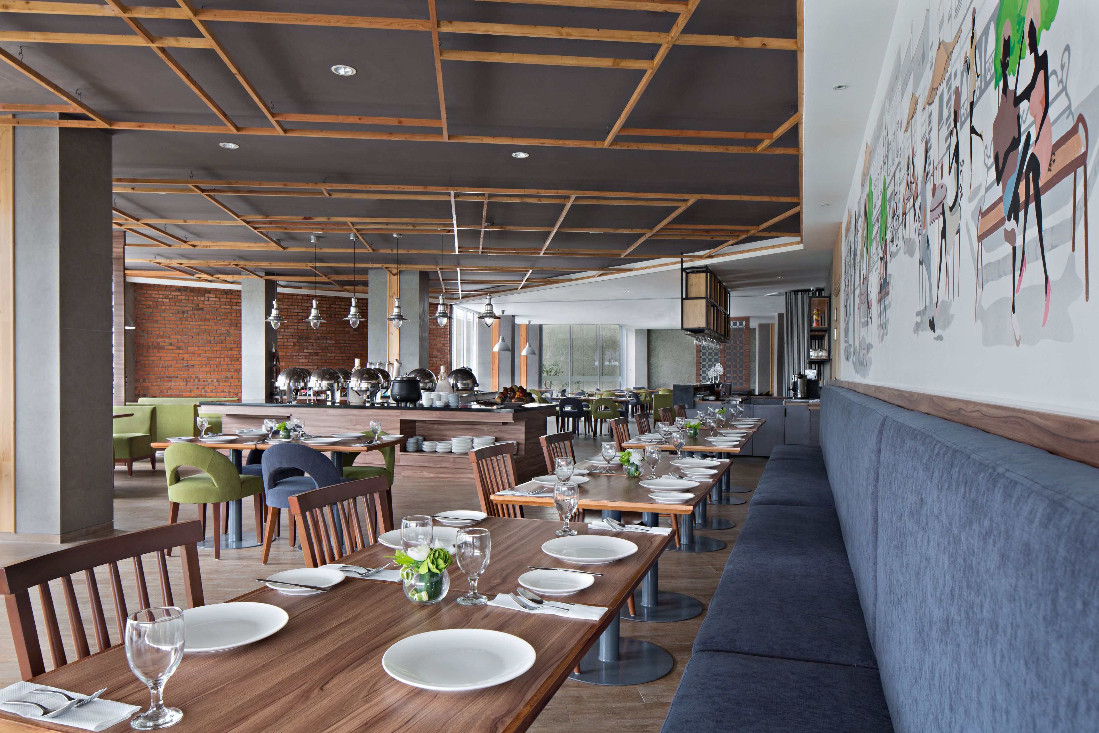 Un restaurant avec des tables en bois, des chaises vertes et un long banc bleu.