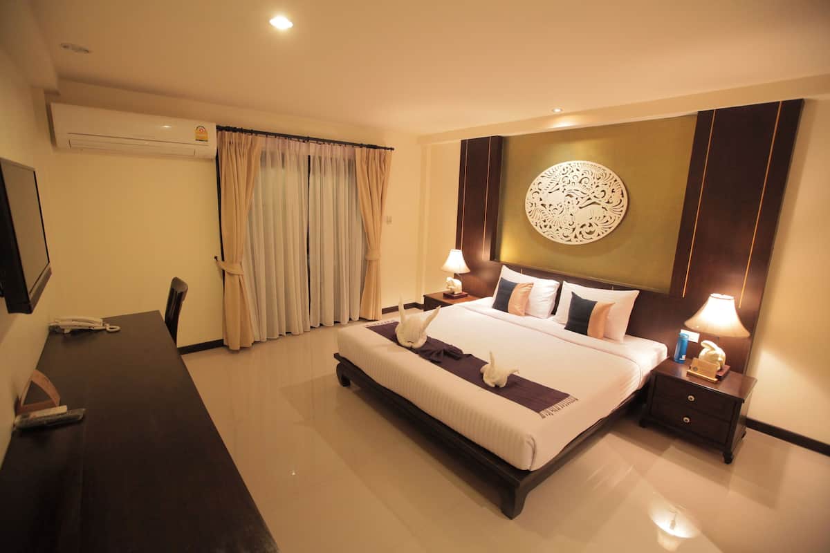 A hotel room with a large bed, bedside tables, a desk, and an air conditioning unit.