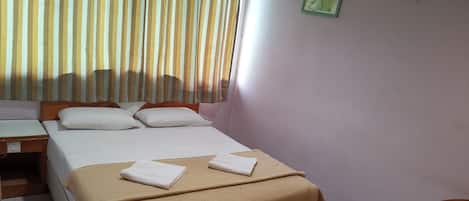 Quarto de hotel bem arrumado, com uma cama, uma escrivaninha e uma cadeira.