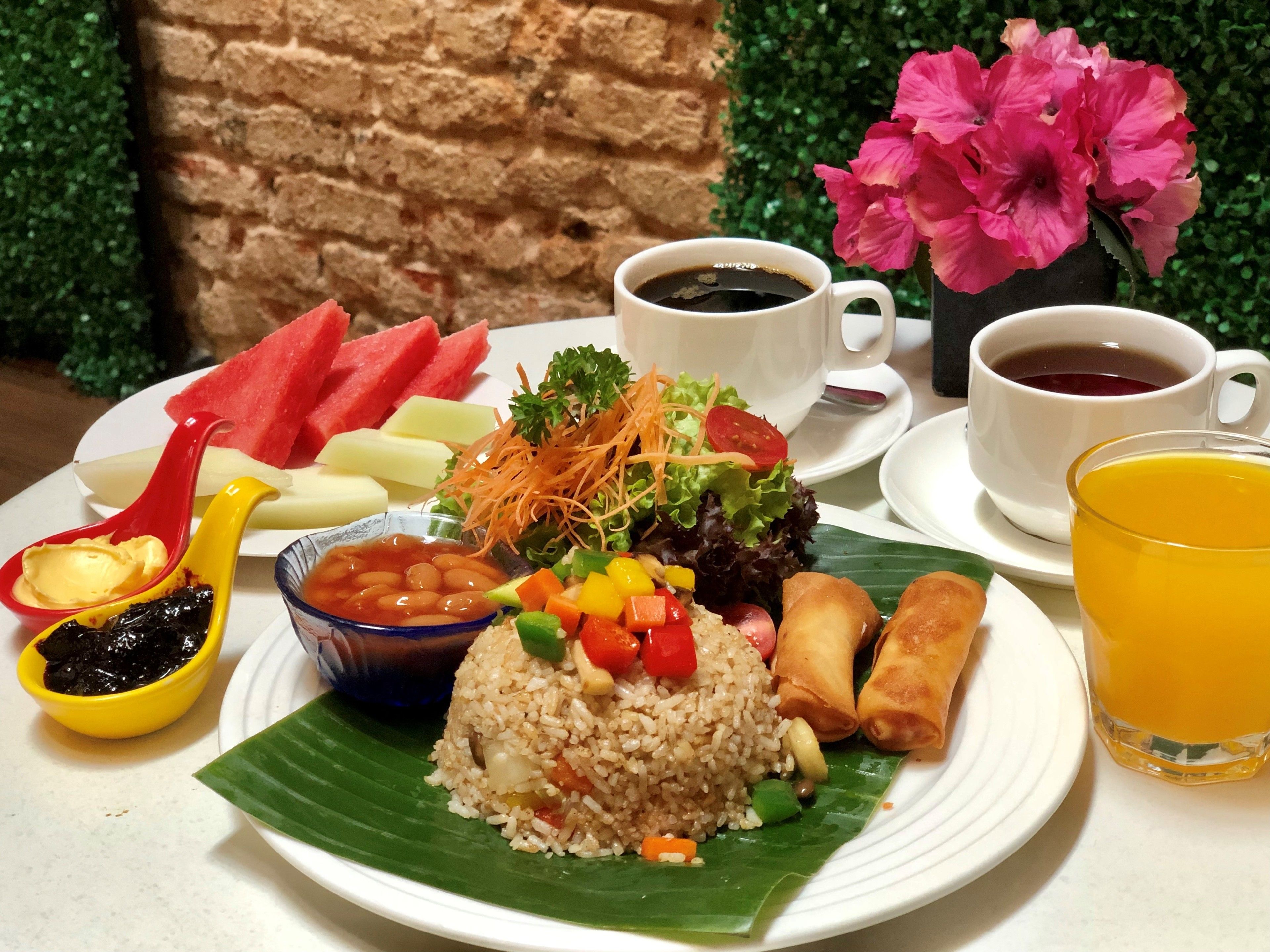 A plate of food including rice, vegetables, and fried items, accompanied by drinks and a flower.