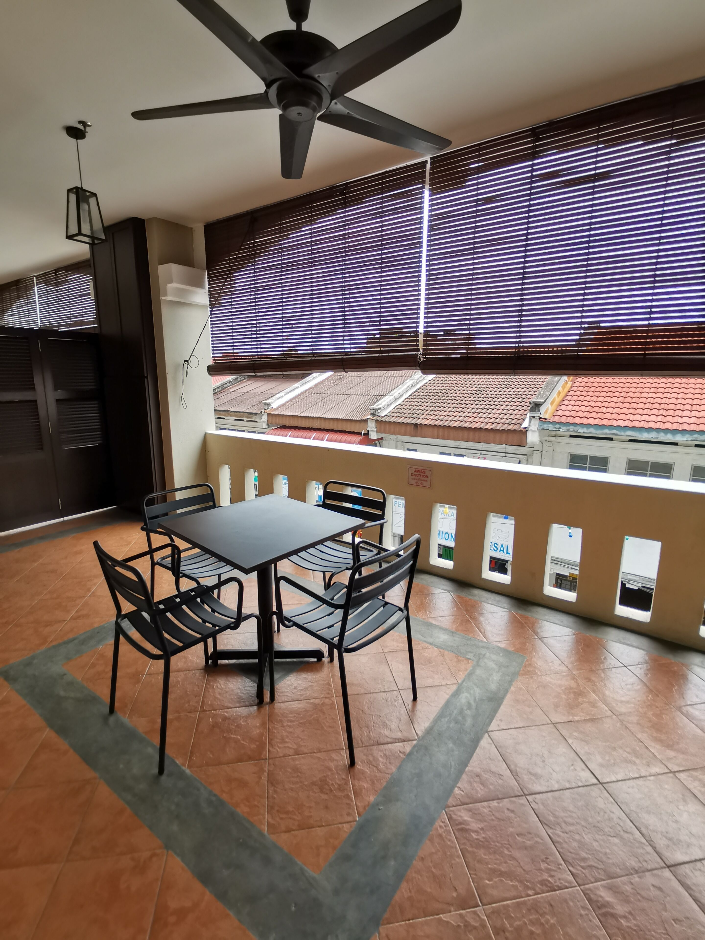 A balcony with a table and chairs, a ceiling fan, and a view of buildings through large windows with blinds.
