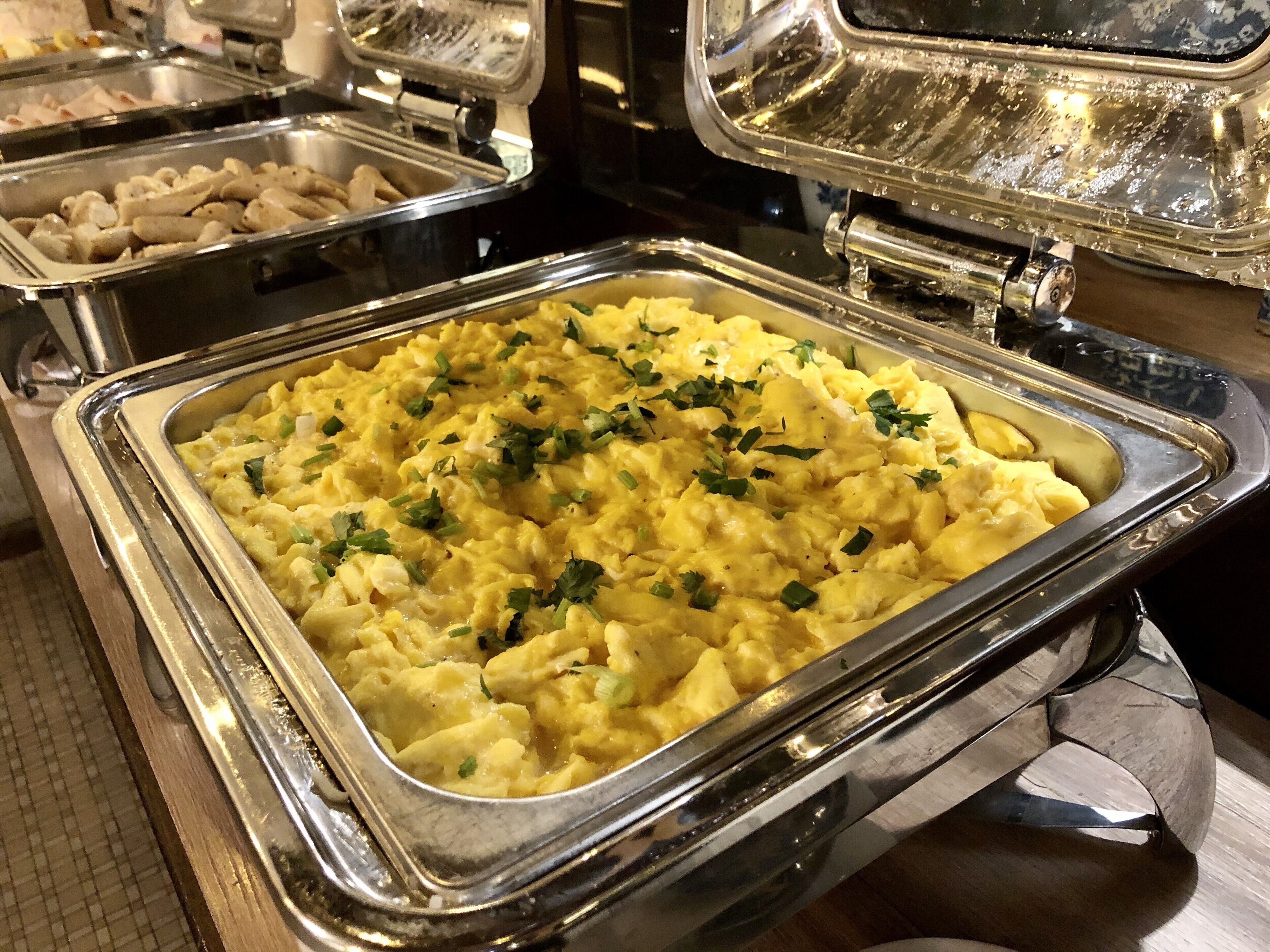 A buffet with various food items, including a large container of scrambled eggs garnished with herbs.