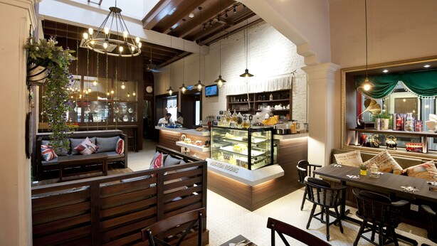 A cozy café with wooden furniture, a central display case, and hanging lights. - Kimberley Hotel Georgetown (George Town)