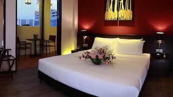 A hotel room with a large bed, a desk, and a chair. There is a view of the city through a window.