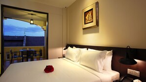 A hotel room with a large bed, a bedside table with a lamp, a phone, and a picture on the wall. There is a window with a view of buildings and a balcony with a table and chairs. - Kimberley Hotel Georgetown (George Town)