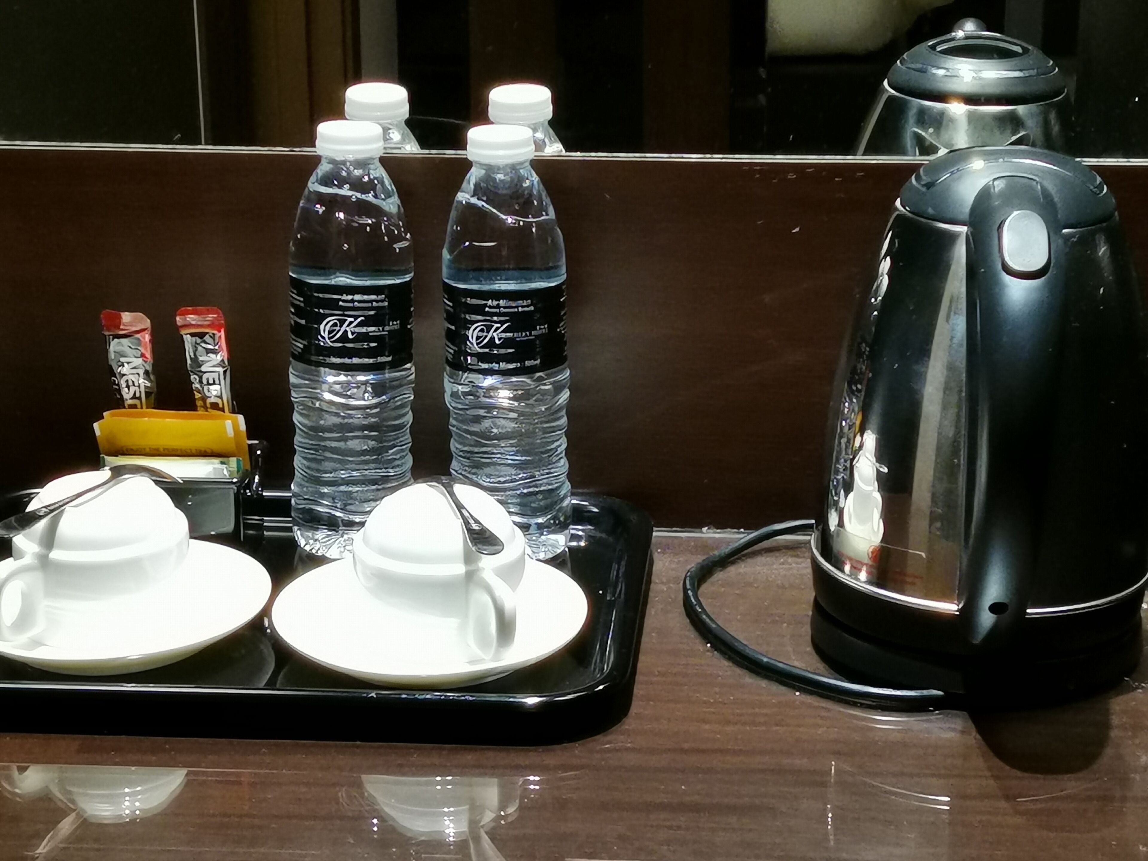 A kitchen counter with a kettle, two bottles of water, a tray with a cup and saucer, and a small container with a spoon.
