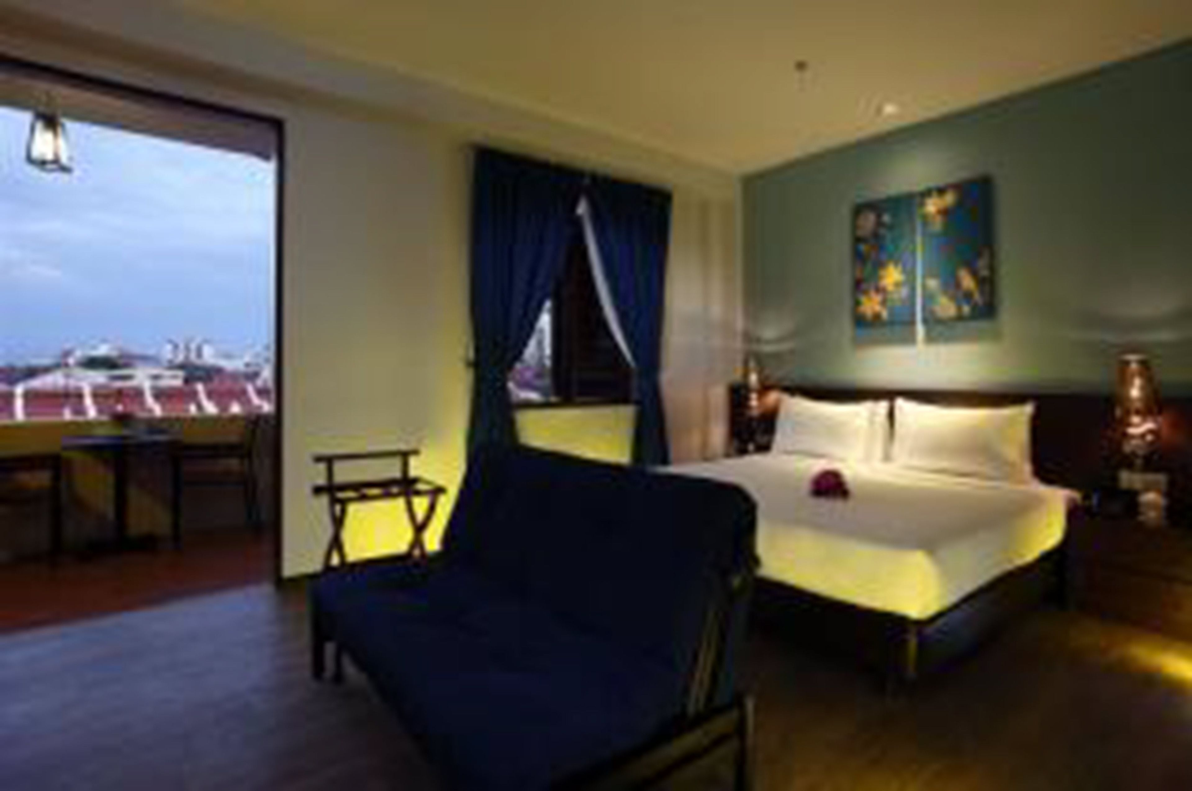 A hotel room with a bed, a chair, a desk, and a window with a view of airplanes.