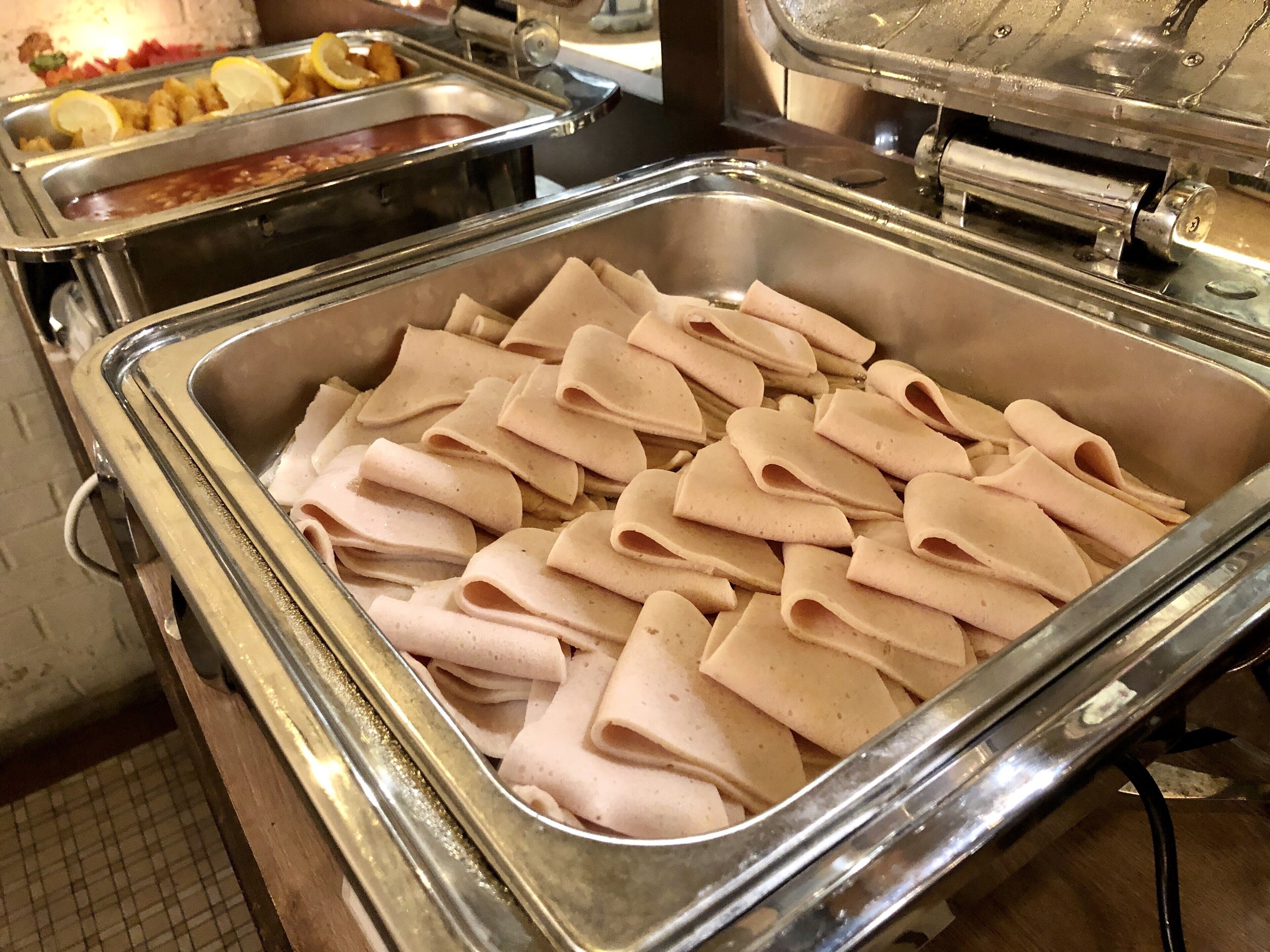 Uma área de buffet com diversas opções de comida, incluindo uma bandeja de carnes fatiadas e um recipiente com pães achatados.