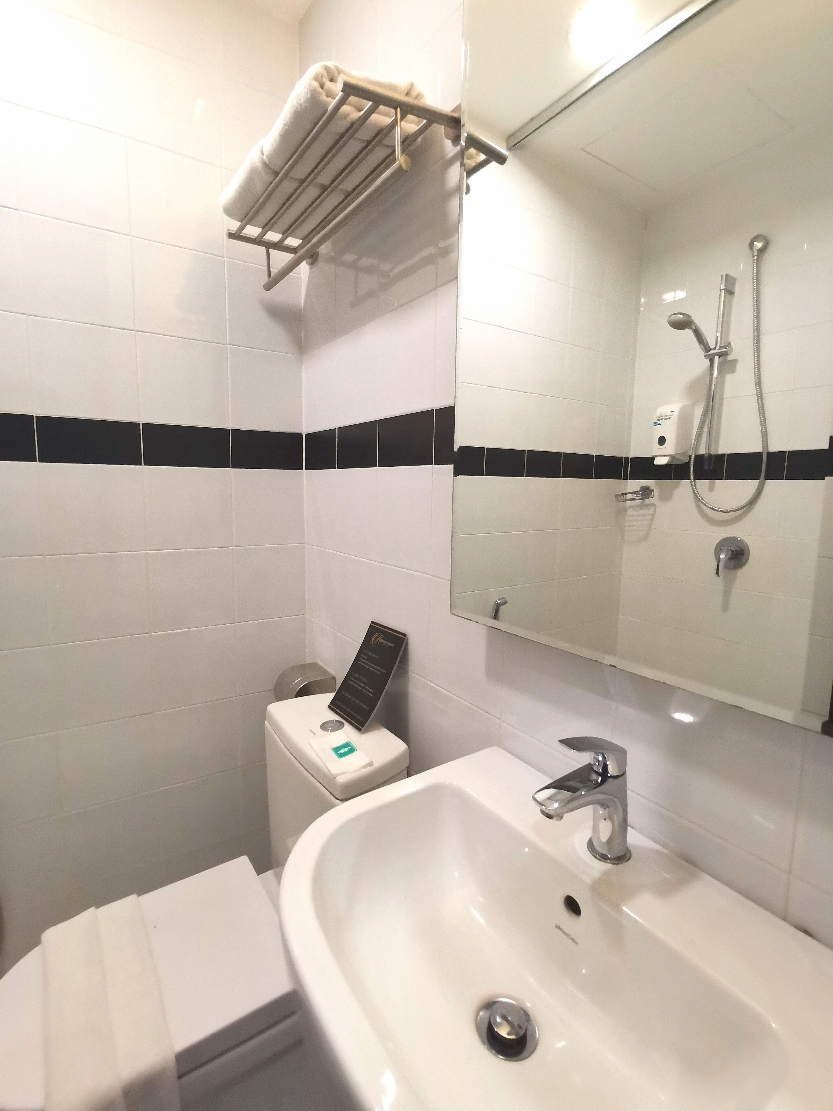 A bathroom with white tiles, a sink, a mirror, a towel rack, and a shower.
