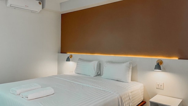 A hotel room with a bed, bedside lamps, a nightstand, and an air conditioning unit. - Baan Nai Wiang (Nan)