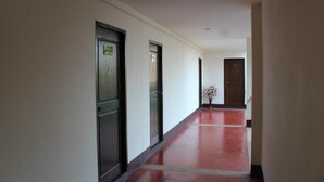 A long, narrow hallway with doors on both sides, a red floor, and a vase with flowers in the center. - Baan Nai Wiang (Nan)