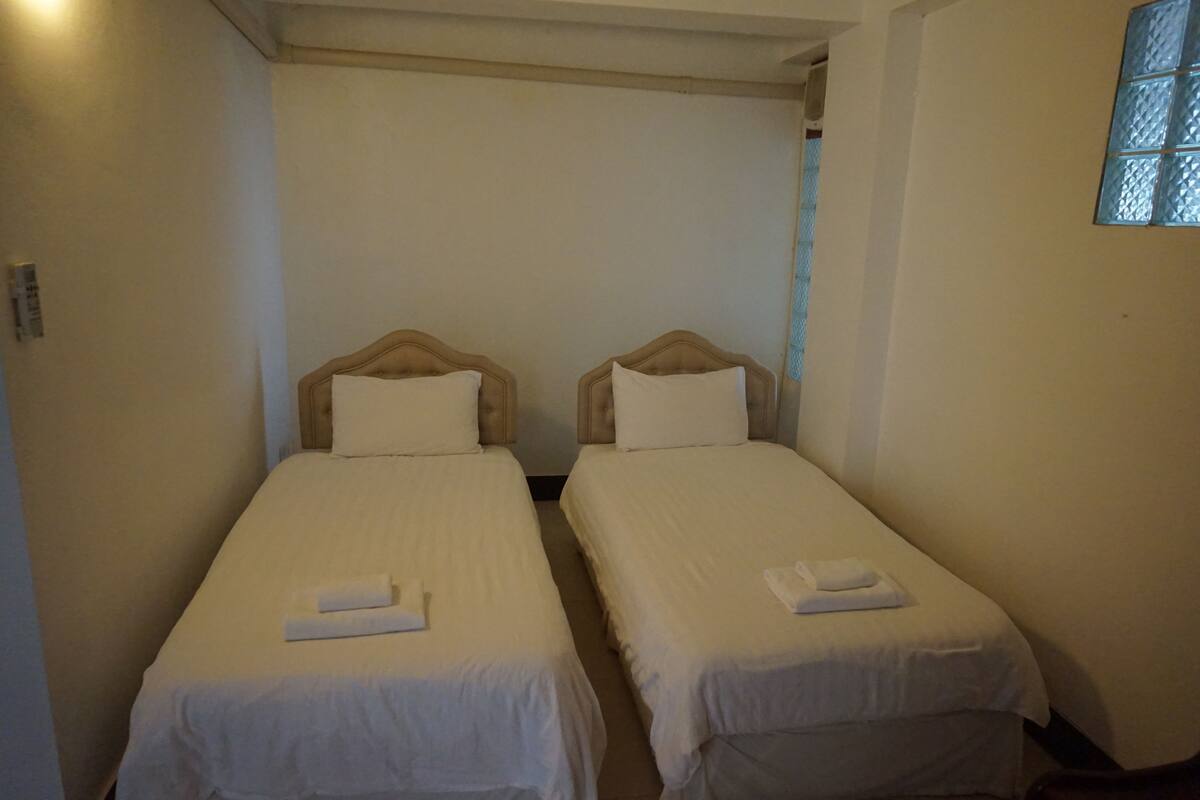 Two single beds with wooden headboards and white bedding, arranged in a narrow room with a window on the right.