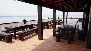 Une terrasse extérieure avec des tables et des bancs en bois, un sol carrelé et une vue sur l’eau.