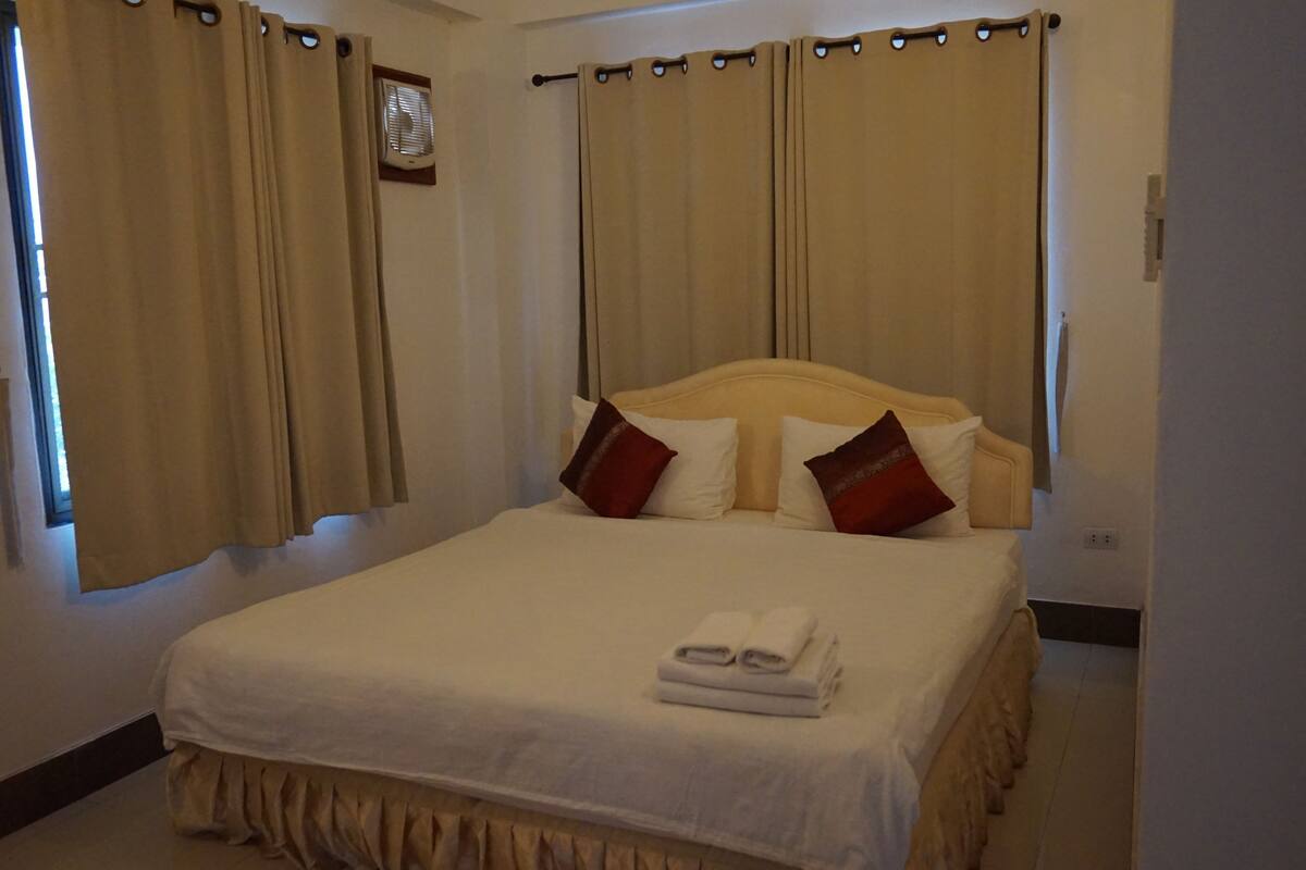 A hotel room with a large bed, beige curtains, and a window with blinds.