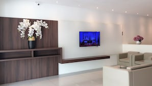 A modern waiting area with a wooden reception desk, a flat-screen TV, and a beige sofa. - Tumike Hotel Bentong (Bentong)