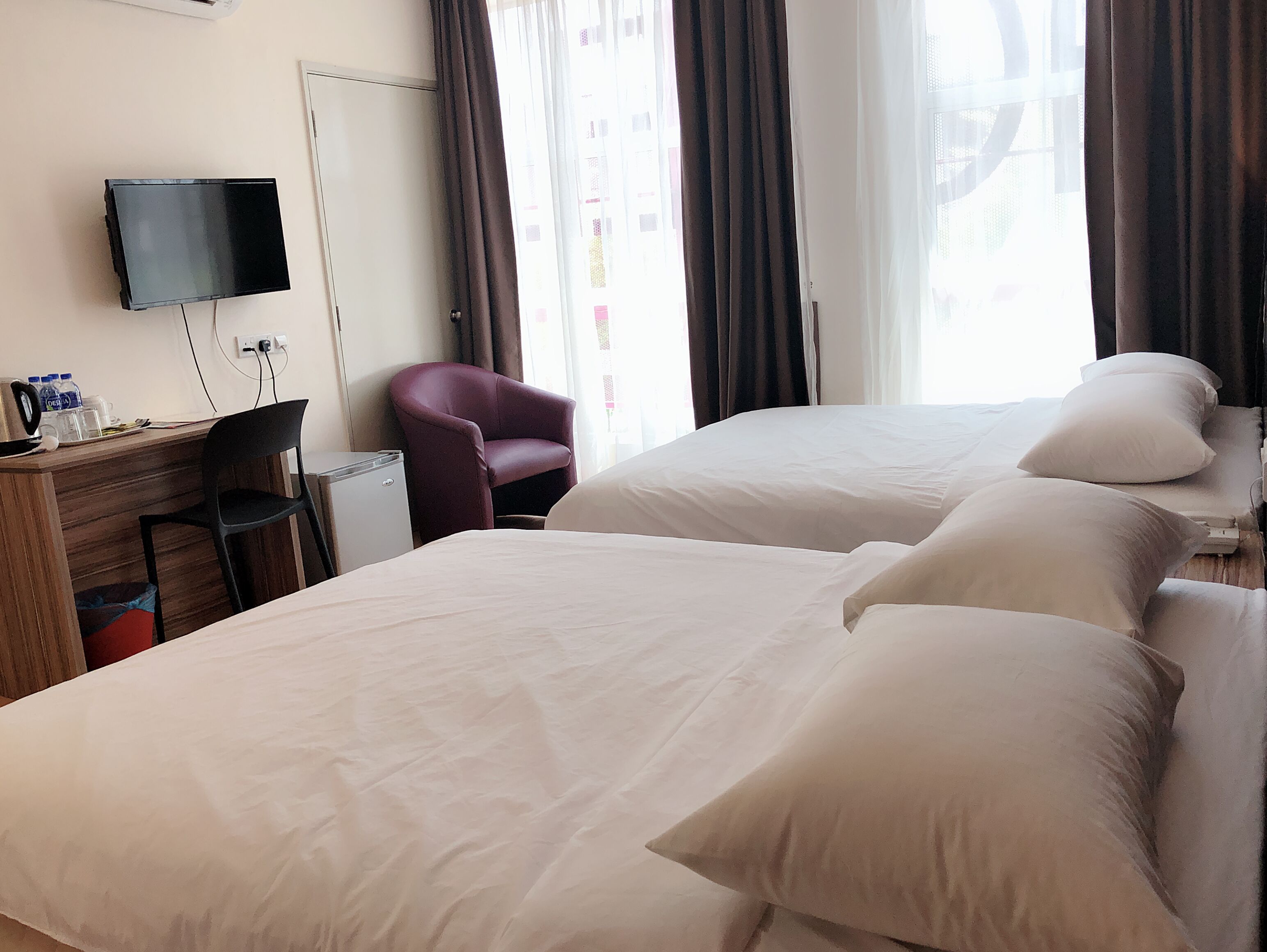 Habitació d'hotel amb dos llits, un escriptori amb cadira, una televisió i una finestra amb cortines.