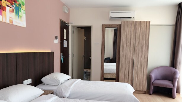 A hotel room with two beds, a wooden headboard, an air conditioning unit, a purple chair, and a mirror. - Tumike Hotel Bentong (Bentong)