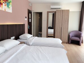 A hotel room with two beds, a wooden headboard, an air conditioning unit, a purple chair, and a mirror. - Tumike Hotel Bentong (Bentong)