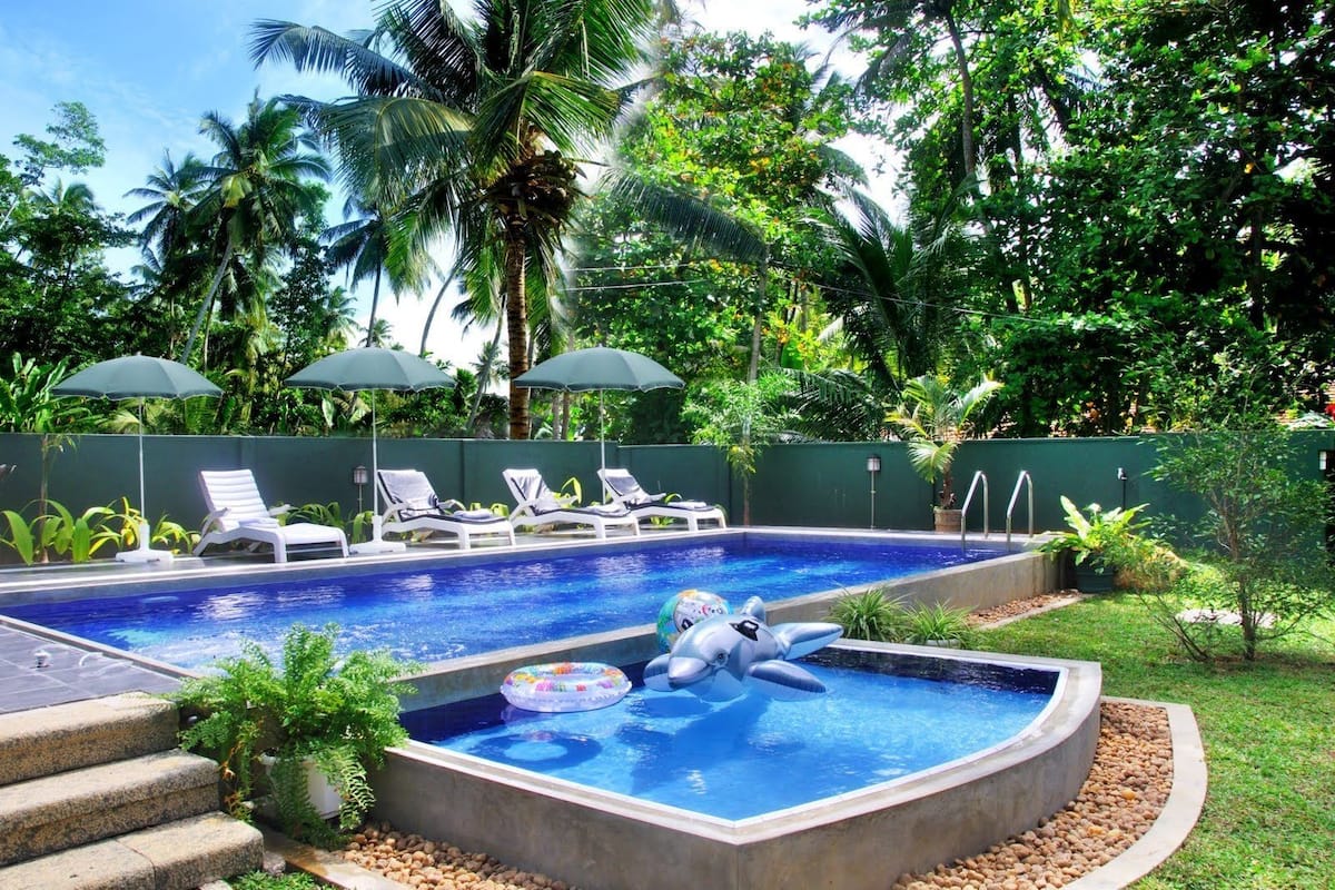 A swimming pool with lounge chairs and umbrellas, surrounded by lush greenery.