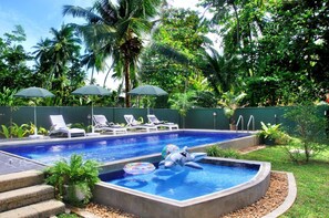 A swimming pool with lounge chairs and umbrellas, surrounded by lush greenery. - Hikka Villa (Hikkaduwa)