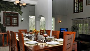 Un comedor con una mesa de madera dispuesta para seis personas, rodeada de sillas, y una televisión y un ventilador al fondo.