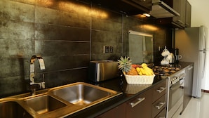 A modern kitchen with stainless steel appliances, a double sink, and a fruit basket on the counter. - Hikka Resort (Hikkaduwa)