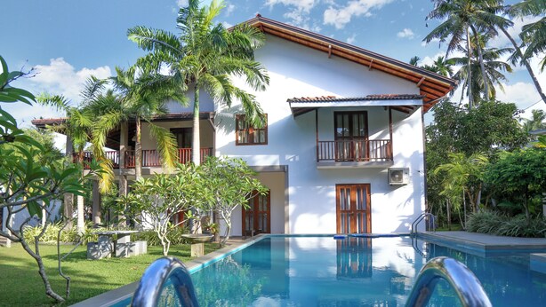 A swimming pool with a metal ladder, surrounded by lush greenery and a two-story building with balconies. - Hikka Resort (Hikkaduwa)