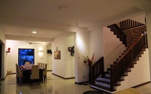 Una sala de estar moderna con comedor, una escalera y una pantalla de televisión grande.