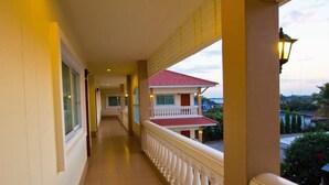 A corridor with a balcony, a view of a red-roofed building, and a lamp post. - Nuntiya Terrace (Udon Thani)