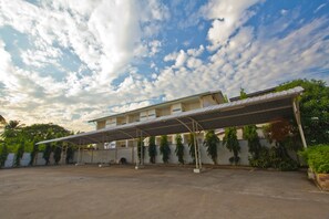 A covered outdoor area with a building in the background, surrounded by greenery. - Nuntiya Terrace (Udon Thani)