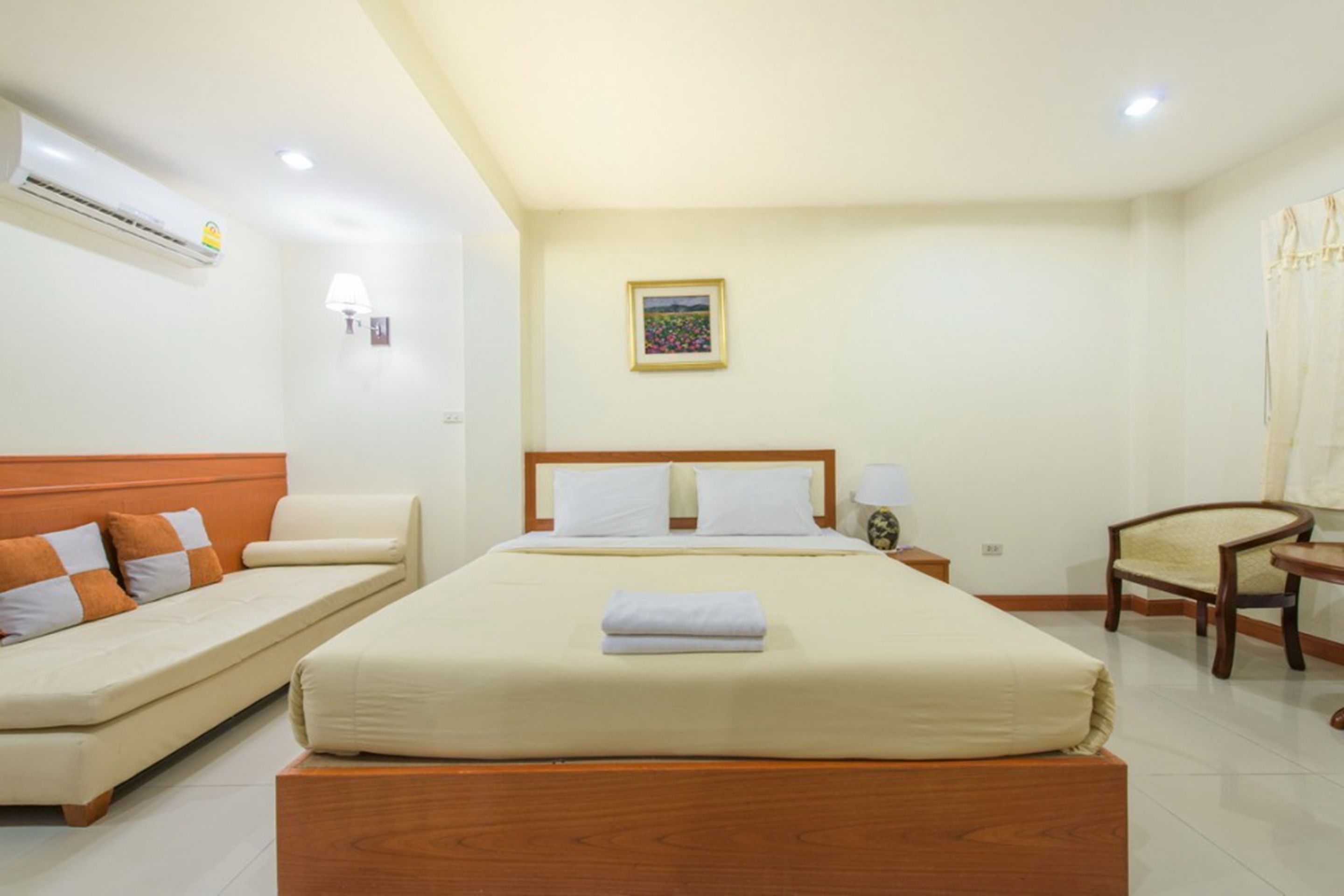 Una habitación de hotel con cama, sofá, sillón, aire acondicionado y un cuadro en la pared.