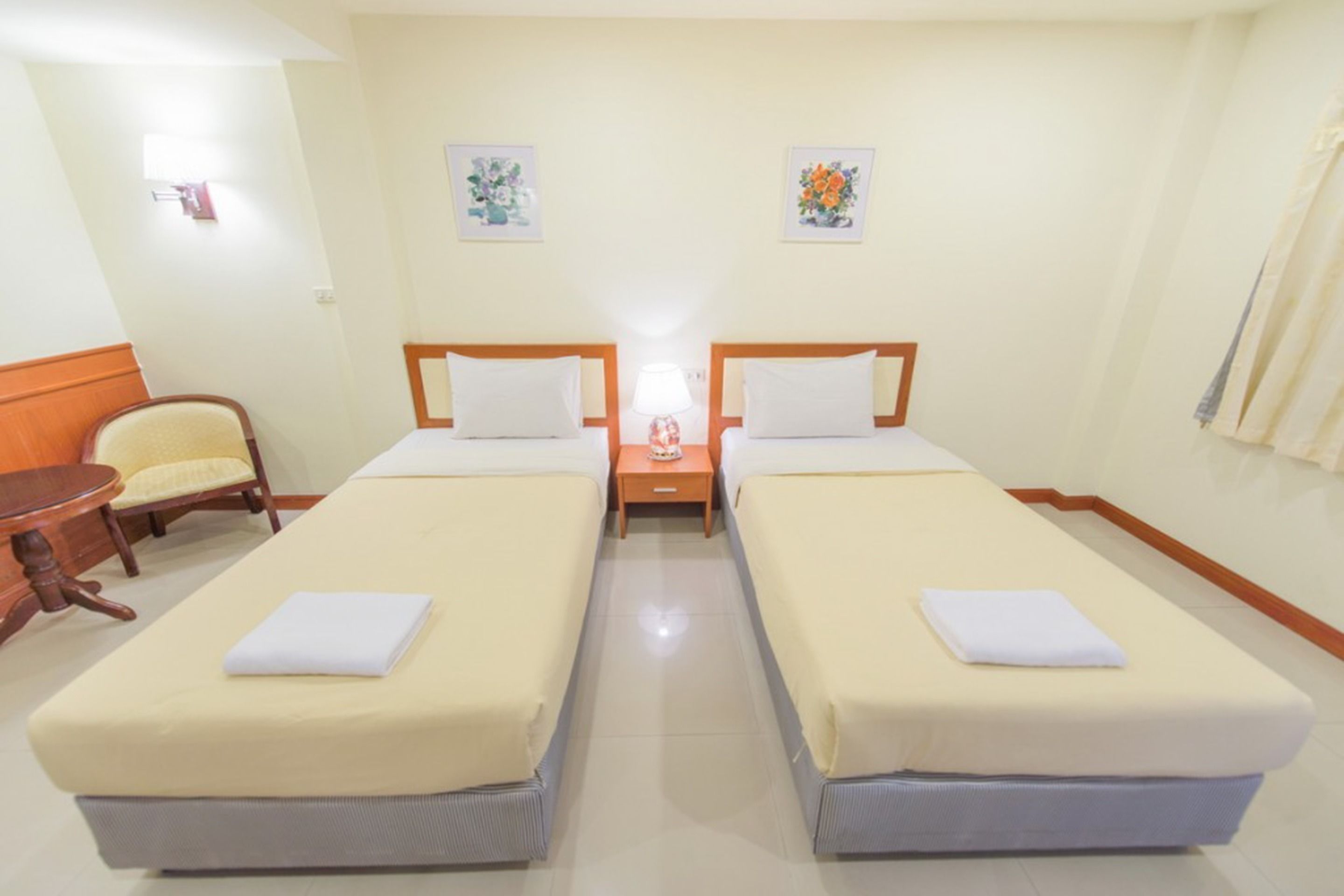A hotel room with two single beds, a small round table, and a chair.
