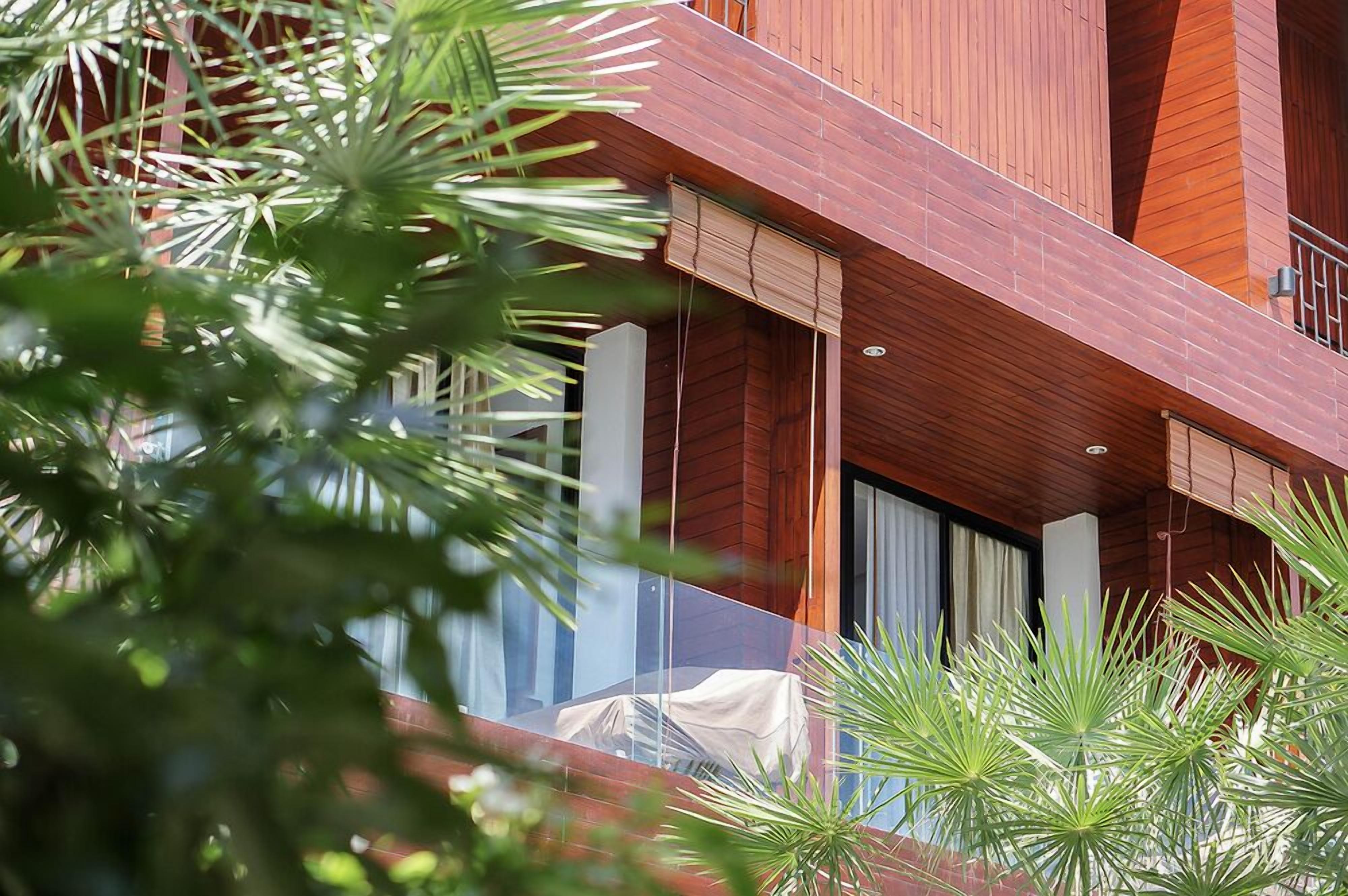 Un edificio moderno con fachada de madera, ventanas grandes y un balcón con zona de estar cubierta.
