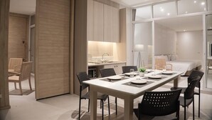 A modern hotel room with a dining area, kitchenette, and a large sliding door leading to a bedroom. - Tri-Shawa Resort (Prachuap Khiri Khan)