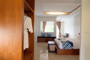 Une chambre avec une armoire en bois, un lit recouvert d’une courtepointe à motifs bleus, un banc et une fenêtre avec des rideaux.