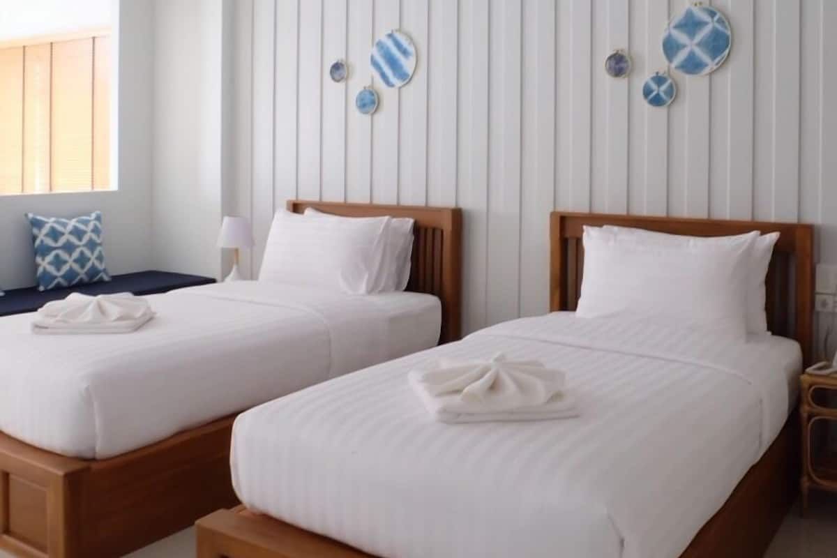 Hotellihuone, jossa on kaksi puista sänkyä, valkoiset vuodevaatteet ja kalteva katto.