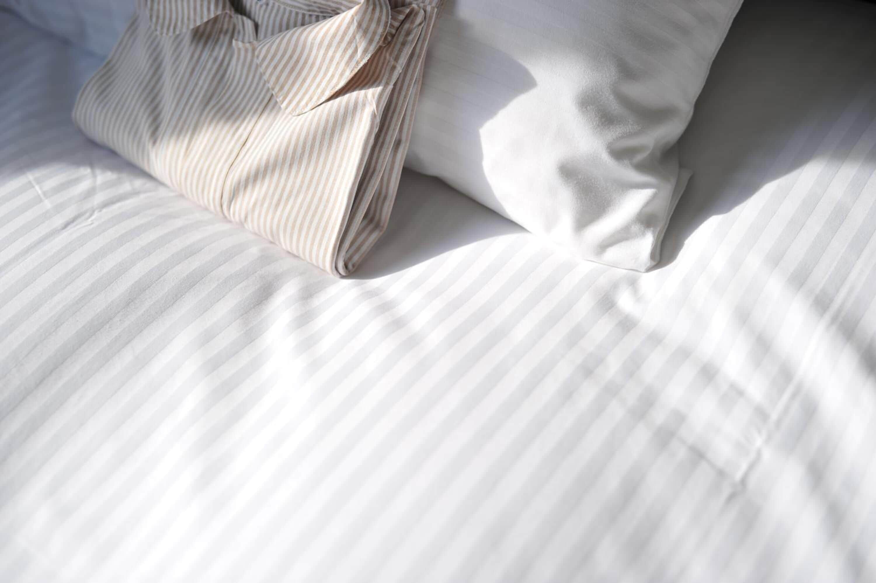 A neatly made bed with striped bedding and a folded shirt on it.