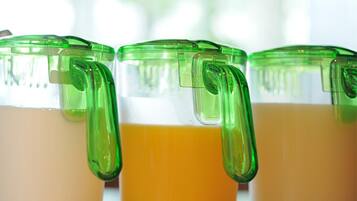 Three glass containers with green lids and handles, filled with a yellow liquid, likely juice or smoothie.