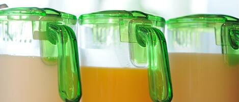 Trois récipients en verre, dotés de couvercles et d’anses verts, et contenant un liquide jaune, vraisemblablement du jus ou un smoothie.