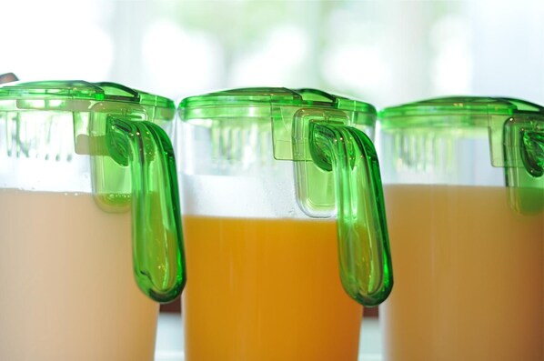Tres recipientes de vidrio con tapas y asas verdes, llenos de un líquido amarillo, probablemente jugo o batido.